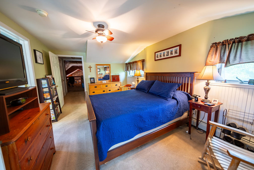 Bedroom with queen bed, dresser and hallway to additional rooms